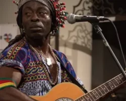 Jimmy Curtis à la guitare électro-acoustique <<Ovation>>. Tenue de Prince bamiléké.